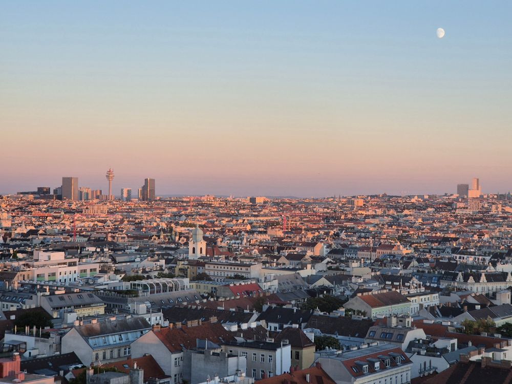weiter Blick über Wien. Der Himmel wird schon leicht orange und rechts oben sieht man den Mond. 