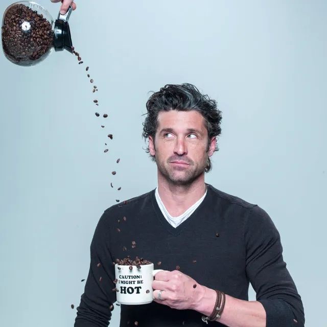 Ein Mann hält eine Kaffeetasse, in die es aus einem Glasbehälter Kaffeebohnen regnet 