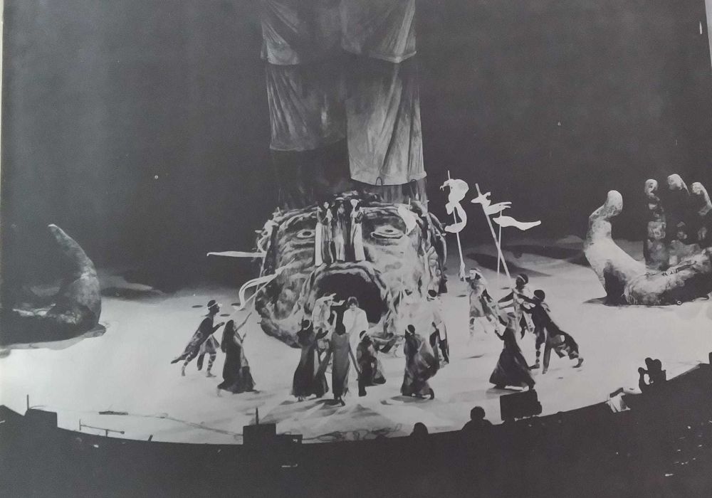 A wide shot of the stage of the 1972 LA production of Jesus Christ Superstar. A huge face, its mouth open wide and its eyes staring upward, dominates center stage. On either side of the stage are huge hands, palms upturned. The aesthetic seems to be evoking prehistoric art, and the vibe is of a giant sinking into the floor, crying out to the sky before it submerges completely. There are people onstage but I have no idea what they're doing, it's really hard to focus on anything but the giant screaming face.