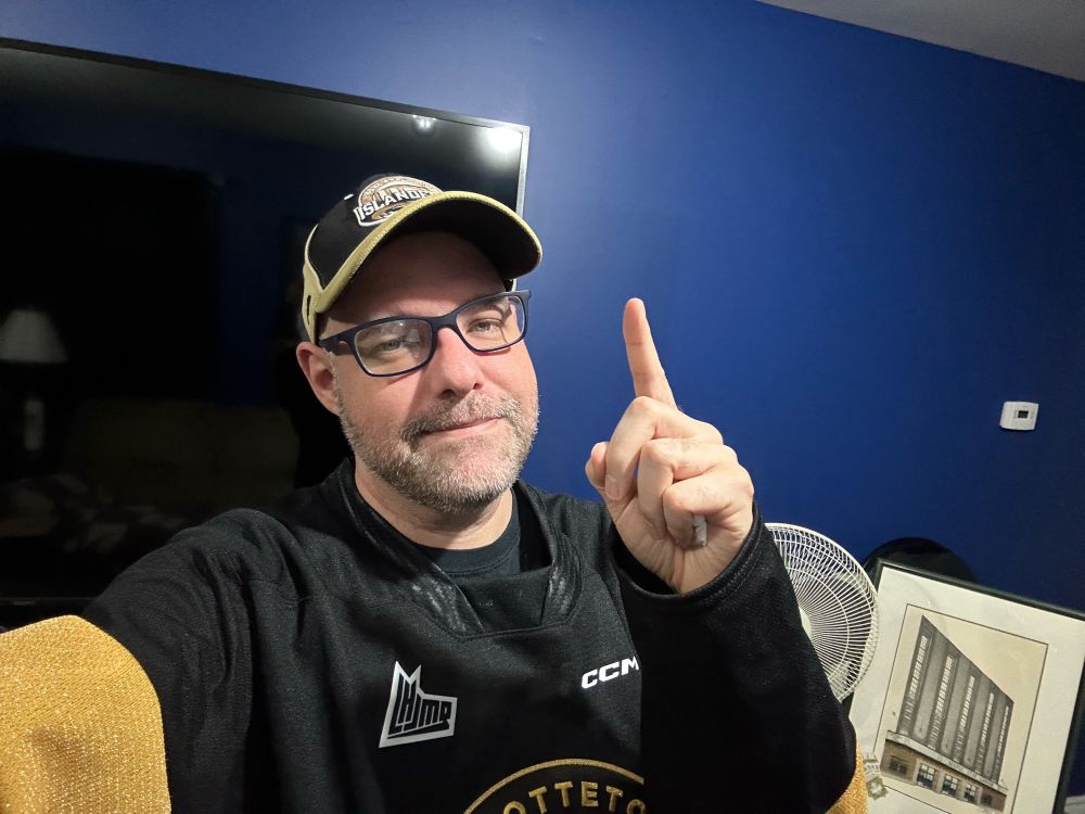 Wearing both an Islanders hat and jersey, pointing one finger to signify Islanders are number 1