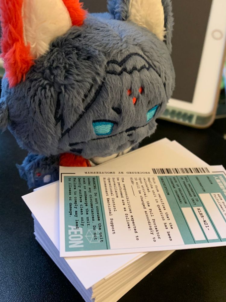 A plush Kolibri that resembles a cat, looking over a stack of small "relocation forms."