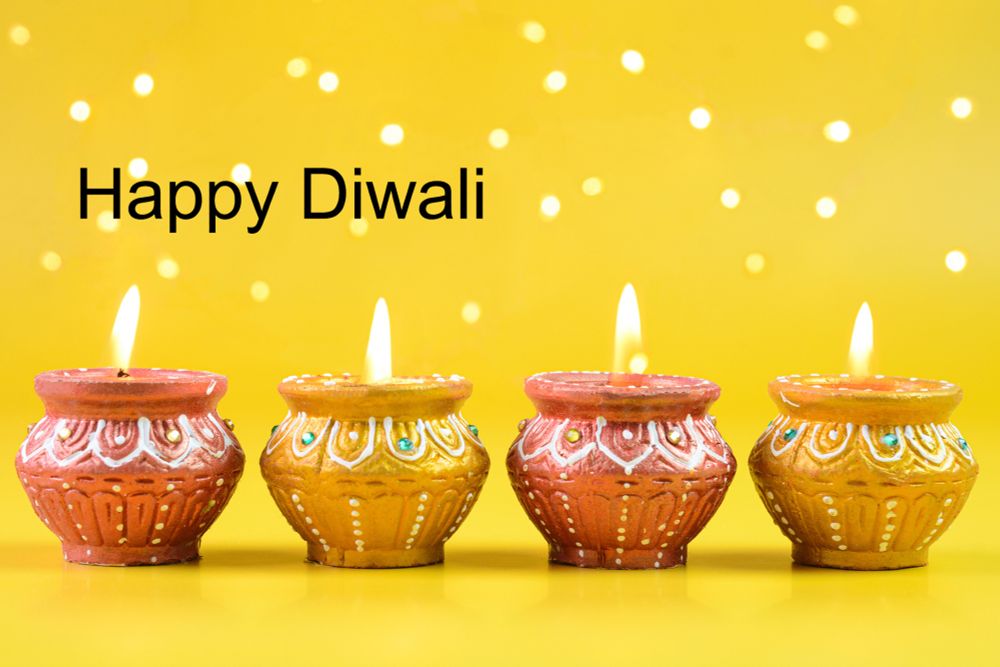 Four lit, brightly coloured candles on a yellow background. The text above reads: 'Happy Diwali'