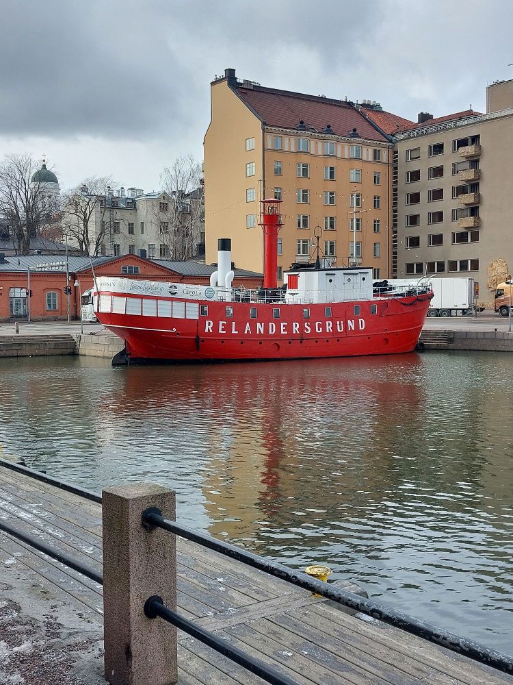 A red and white boat on the water near Helsinki harbour, with a yellow building in the background 