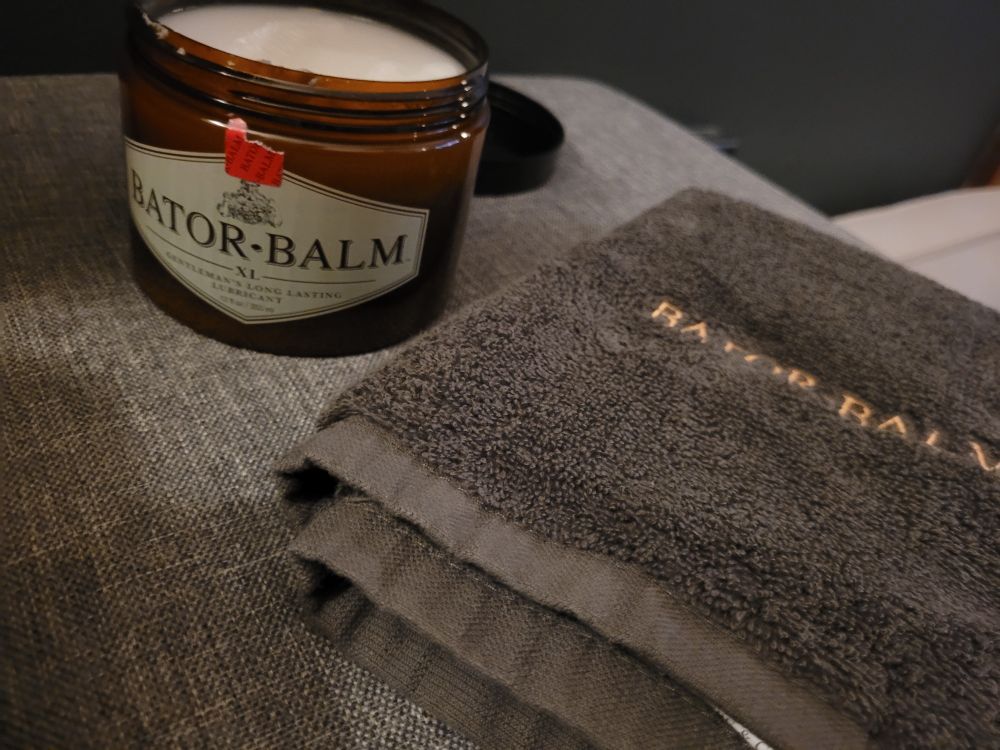 Open tub of Bator Balm sitting next to a Bator Balm towel. 