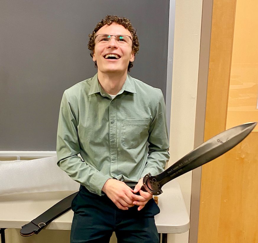 Evan's PhD graduation sword says 'Tamer of Elp3'.