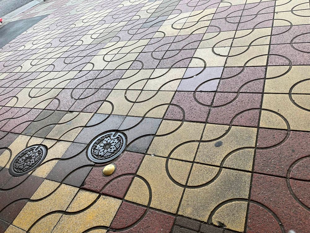 A photo of a pavement tiled in red and yellow with a regular truchet pattern arranged to make repeating bone shapes. 
