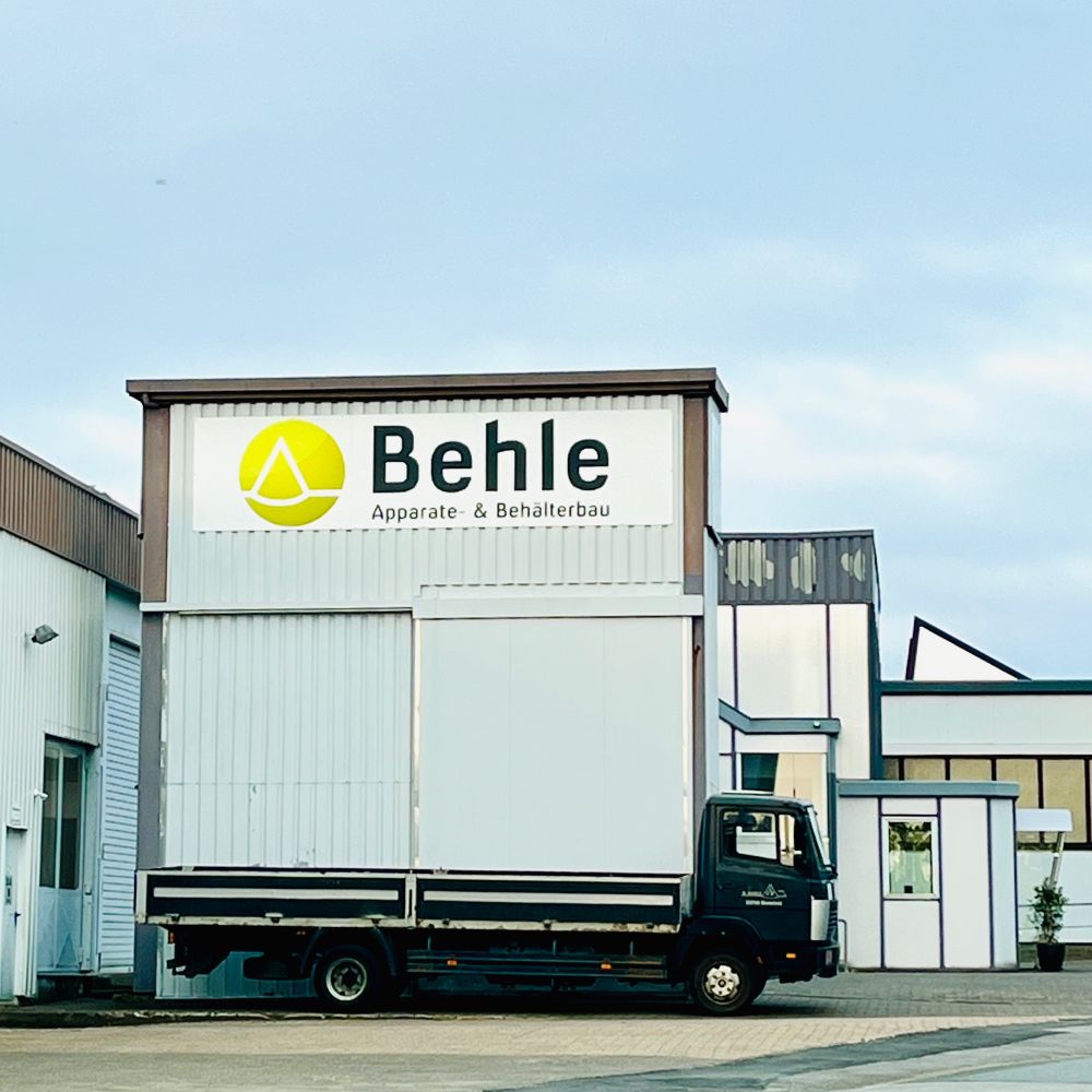 Transporter steht vor einer Werkshalle, die Perspektive lässt die Halle wie einen Aufbau des Wagens erscheinen.