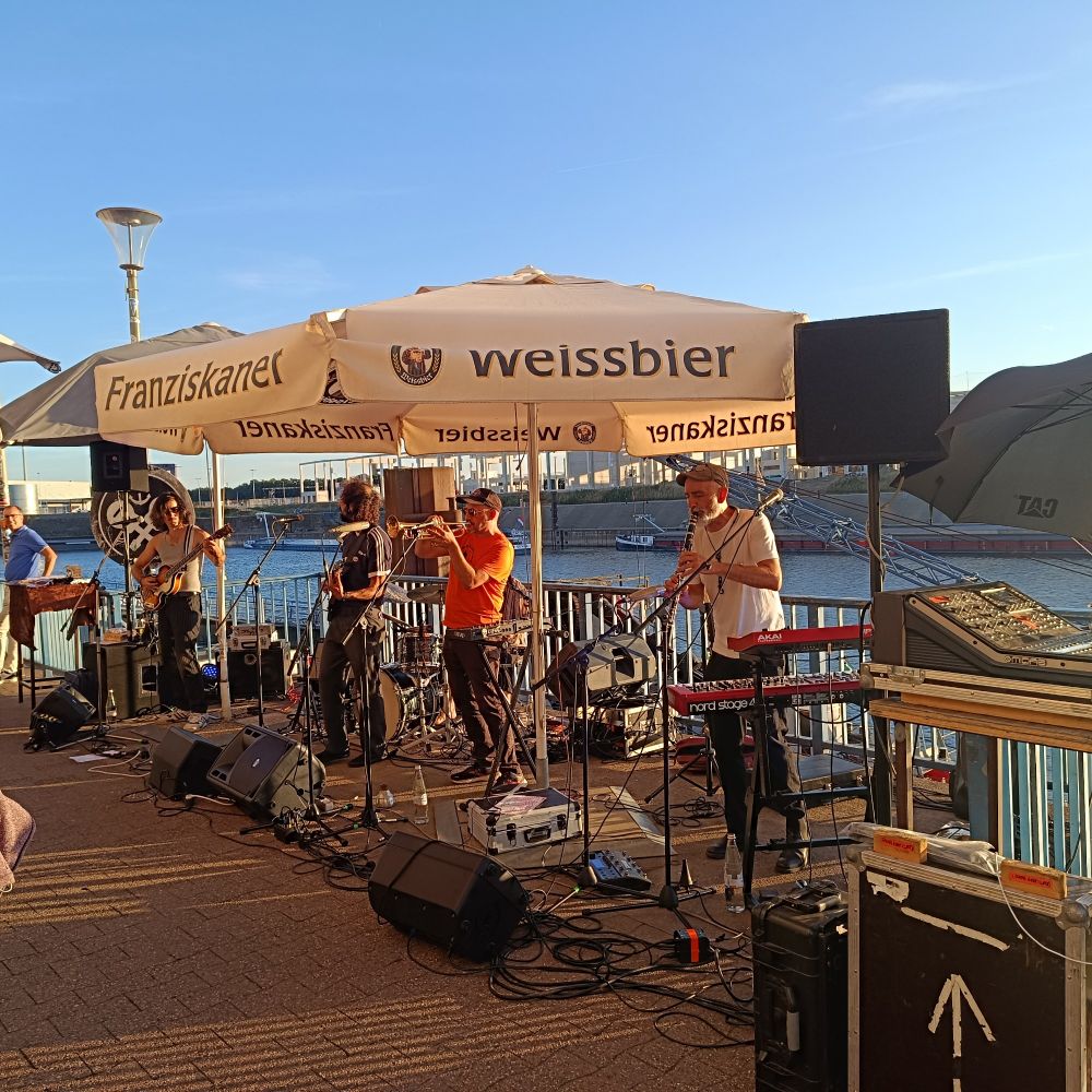 Zu sehen ist die Band, vor dem Hafenbecken an hübis'. In Hintergrund der blaue Abendhimmel