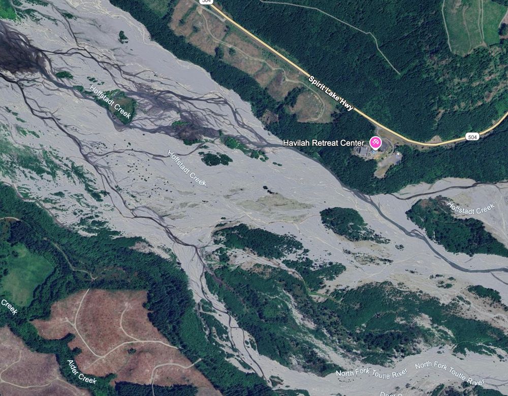 Aerial view of the same reach of the North Fork Toutle River valley near Hoffstadt Creek. By 2023, decades of sediment accumulation have nearly erased the Camp Baker site beneath reworked volcanic deposits. Taken July 2023. Google Earth imagery.