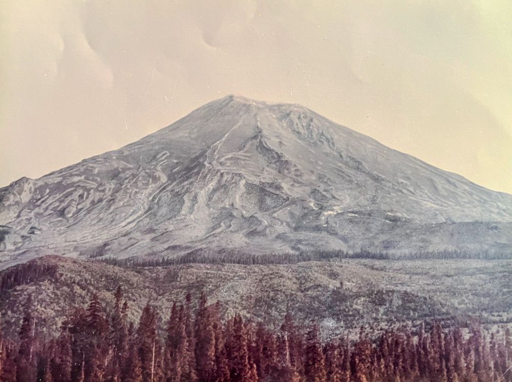 Mount St. Helens as it appeared on the morning of May 18, 1980, viewed from the south. The symmetrical summit is dusted in ash, with deep grooves from weeks of steaming and minor activity visible down the flanks. 

Photo by Kevin Millican.
