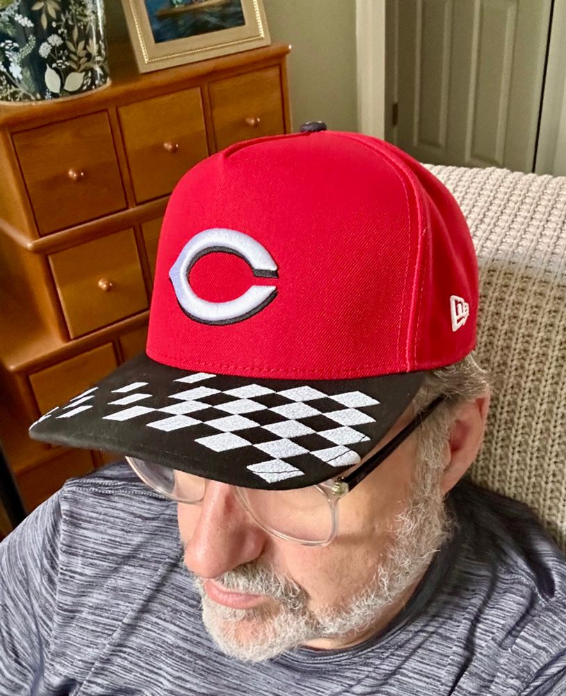 Old man in Cincinnati Reds hat with checkered flag pattern bill. 
