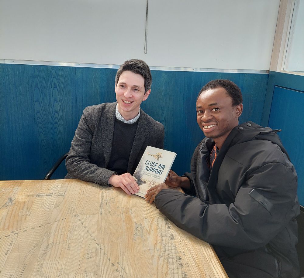 Harry Raffal and Samuel Oyewole sat at a table holding the book: Close Air Support