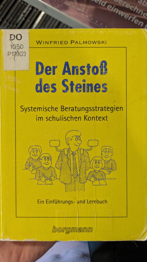 Ockergelbes Cover des Buchs "Der Anatoß des Steines. Systemische Beratungsstrategien im schulischen Kontext. Ein Einführungs- und Lehrbuch" von Winfried Palmowski. Als Illustration dienelt die Comiczeichnung vierer Schüler*innen und eines Lehrers. Letzterer steht den Schüler*innen mit Rücken zugewandt und hat auf den Schultern zwei Rückspiegel wie ein Auto.