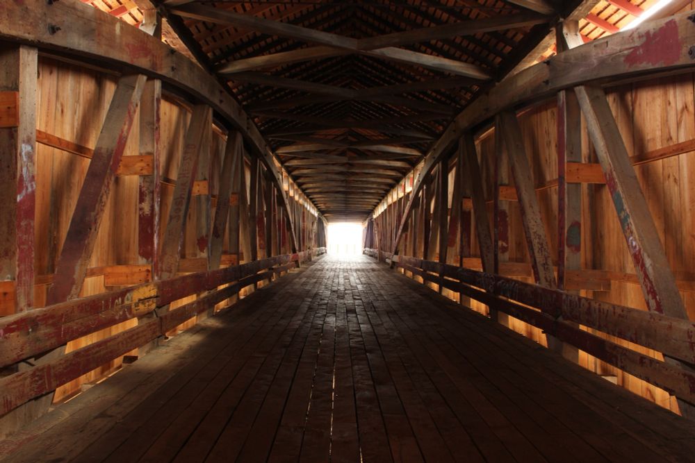 A color picture of the interior of a covered bridge with light shining from the other end.