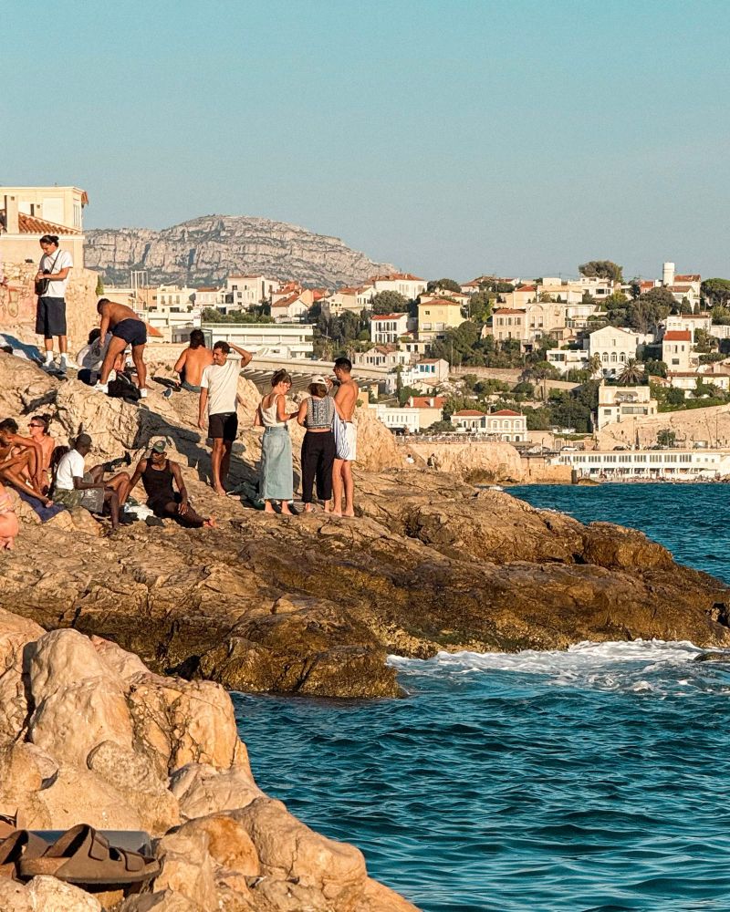people stood on the rocks by the sea at sunset