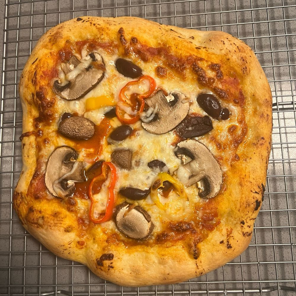 a perfectly baked pizza with mushrooms, peppers, and olives, fresh out of the oven and on a cooling rack.