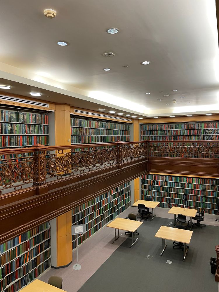 Photo of a room in a library. There are two floors of full bookshelves and a fancy balcony railing 