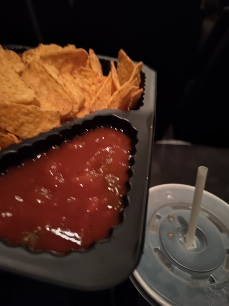 Eine Packung Nachos mit Salsa Sauce und ein Becher Cola im Kino