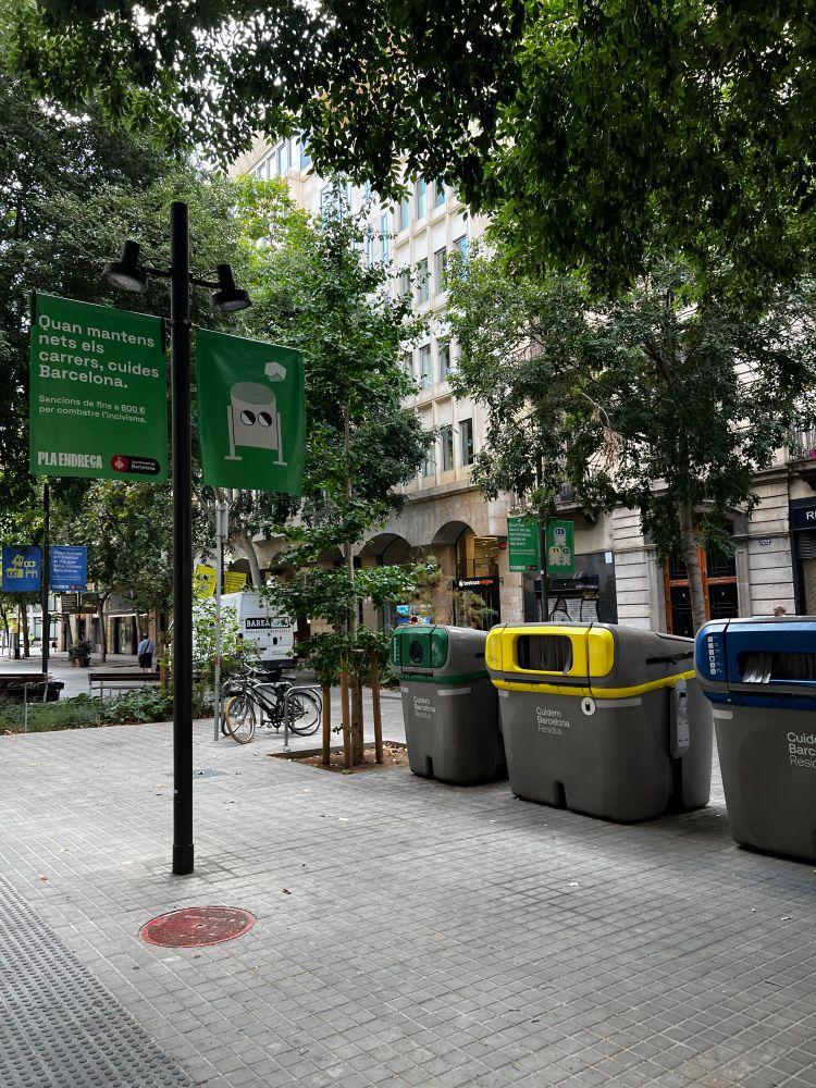 A pedestrian street with three extra large bins labeled for recycling, green waste and non-recyclables. The street is free of garbage.