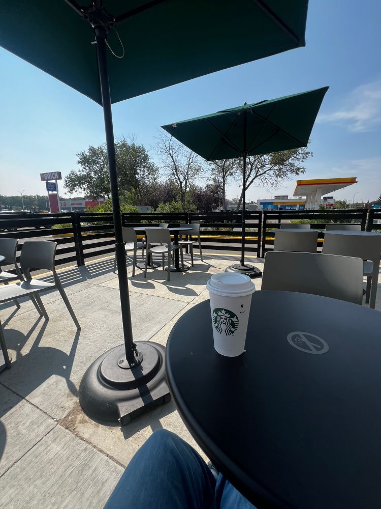 Starbucks coffee cup on a table. Empty patio. No plants or landscaping. Gas station and big box furniture store in the background 