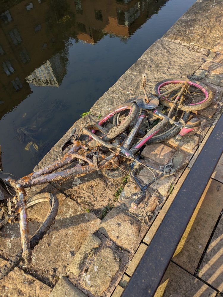 Two muddy bikes, one heavily rusted, by the side of the Manchester canal from which they've just been pulled