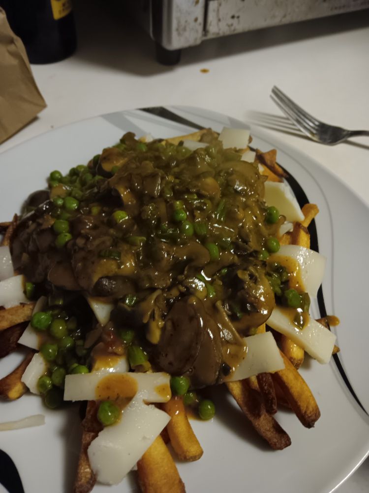 Close up of mushroom gravy poured over well done fries and slabs of white cheese on a white dinner plate