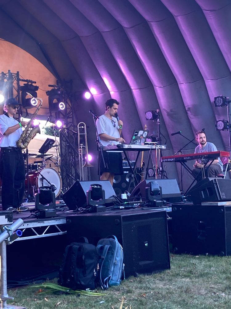 Band on stage with saxophone, trombone, mixing deck, keyboard and drums