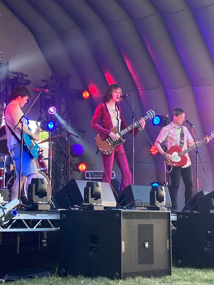 Rock band the bad kissers performing on stage with Connor in the centre in revealing velvet jumpsuit 