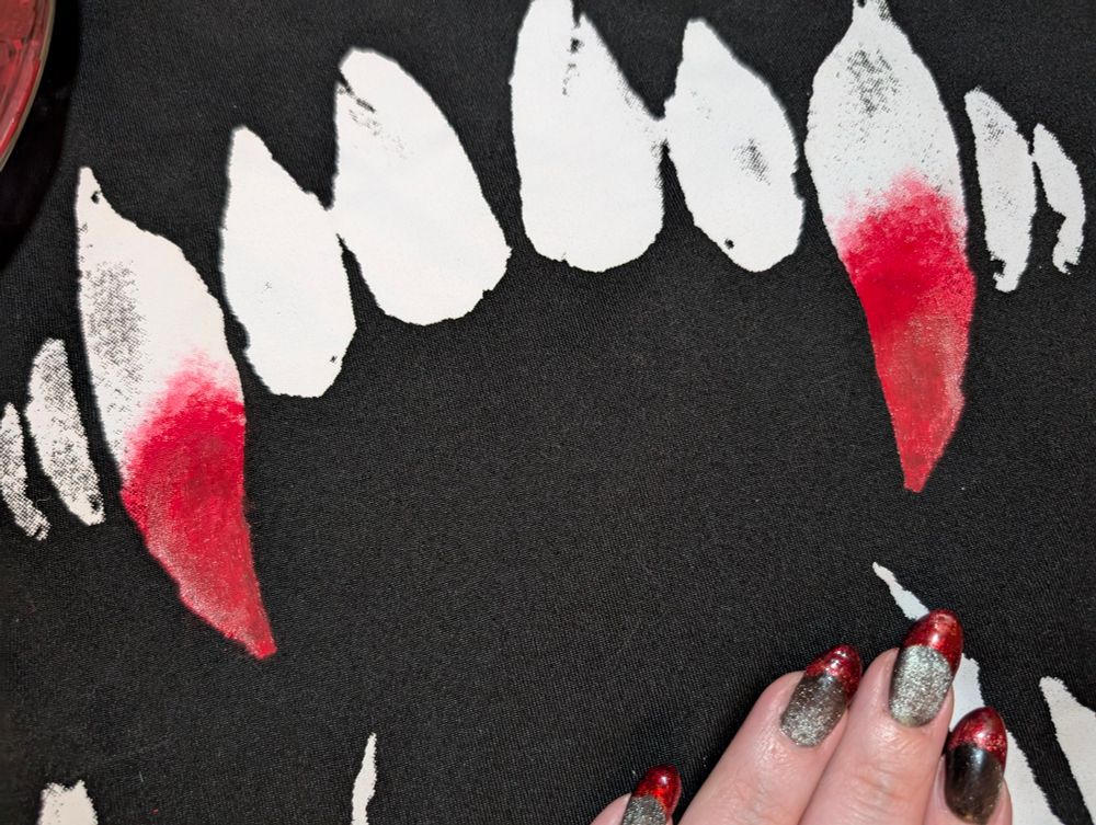 a closer photo of a black shirt with white teeth on it - there's a pain palette beside it and the tips of the canine teeth have been painted red 