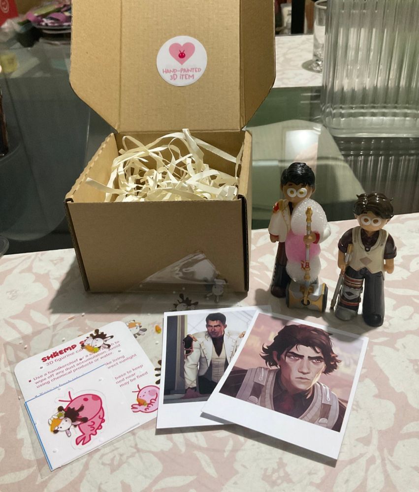 Photo of the care guide, freebies and polaroid prints that come inside the box when you purchase the 3D figurines of Jayce and Viktor.