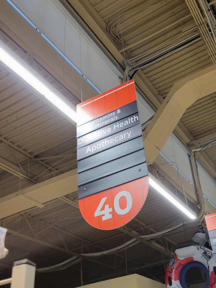 a hanging sign for a grocery aisle, reading from top to bottom: "Vitamins & Minerals", "Digestive Health", and "Apothecary", the last of which is strange for a grocery store