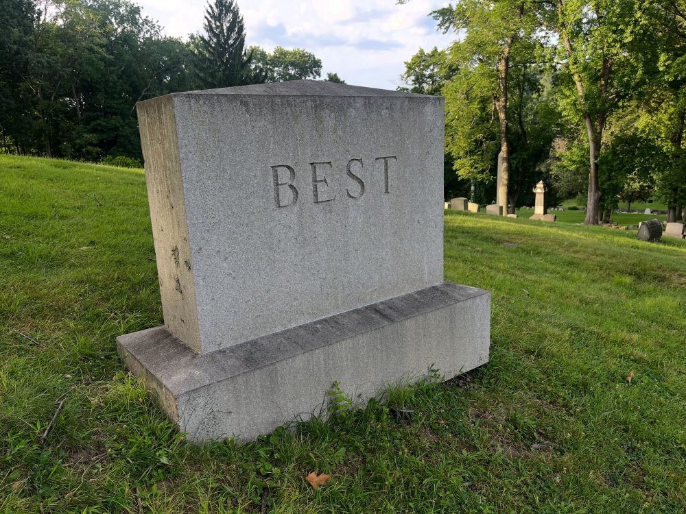 A headstone in a cemetery on a grassy hill, carved with the name “BEST”