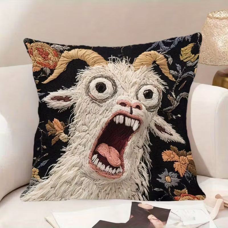 A black pillow on a white couch. The pillow is embroidered with the face of a screaming goat, eyes bulging and mouth wide in an expression of unmitigated horror.