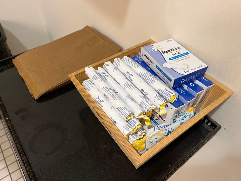 Close-up view of a table in a public restroom with a basket full of feminine products next to a stack of paper bags.