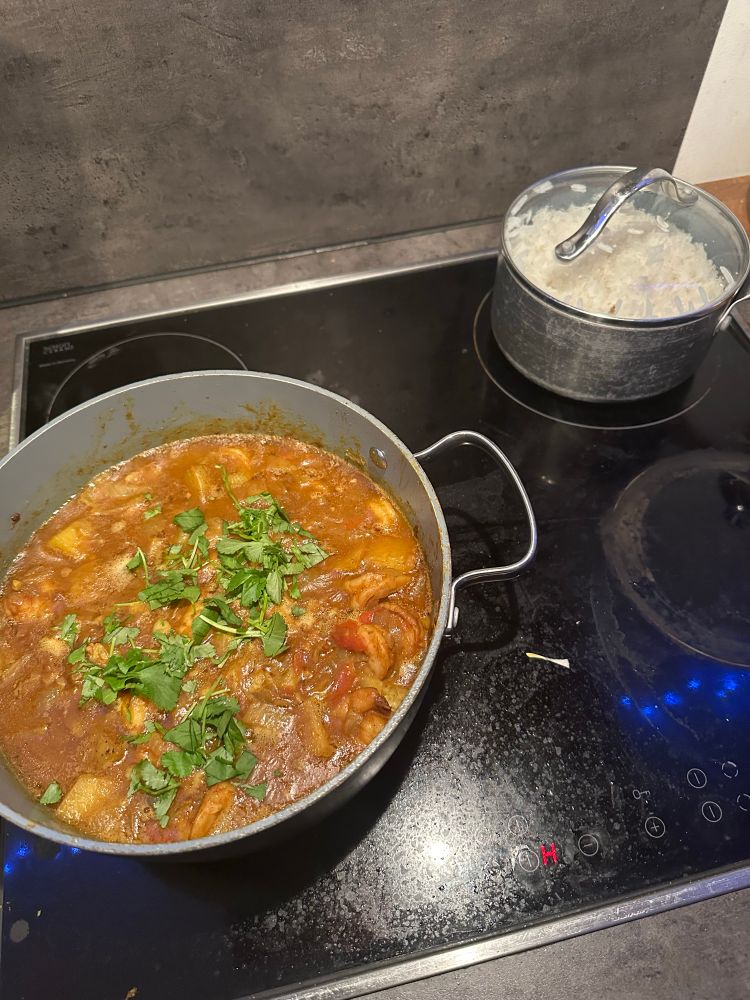 Two pots on a black electric stove top. The one on the left and the bigger of the two has shrimp curry with a cilantro garnish. The curry has potato in it. It’s a Fijian interpretation on Indian curry. The other pot has basmati rice. 