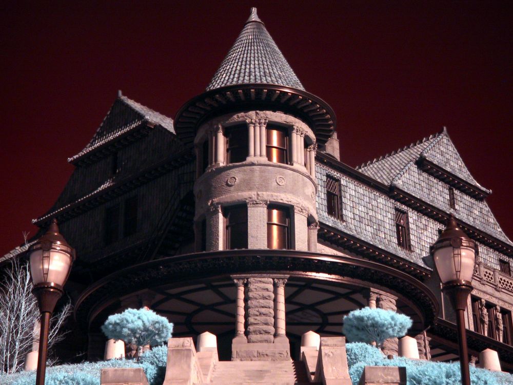 False-color infrared building with dark red sky and turquoise plants. 