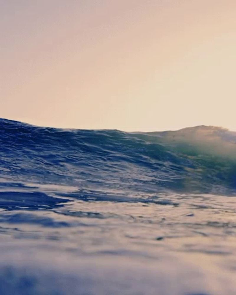 a large wave in the ocean with mountains in the distance