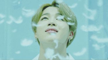 Jimin looking up smiling with feathers falling on him