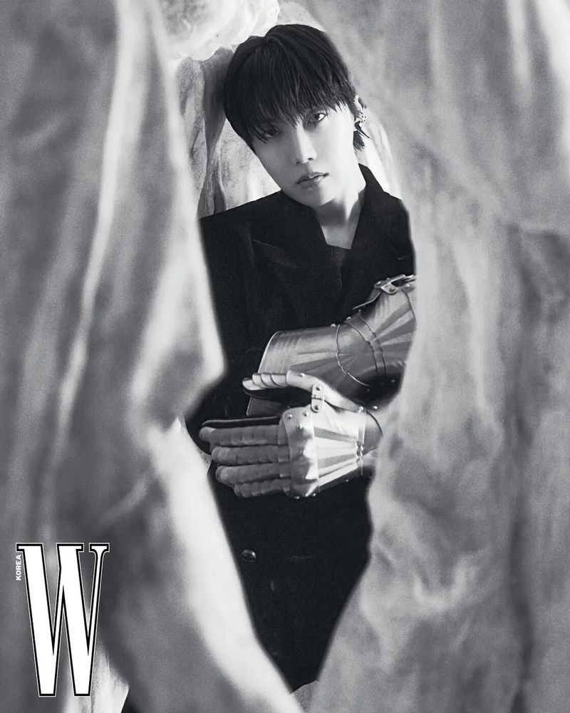 A black and white photo Jhope of BTS. He is wearing a black outfit and silver gloves.