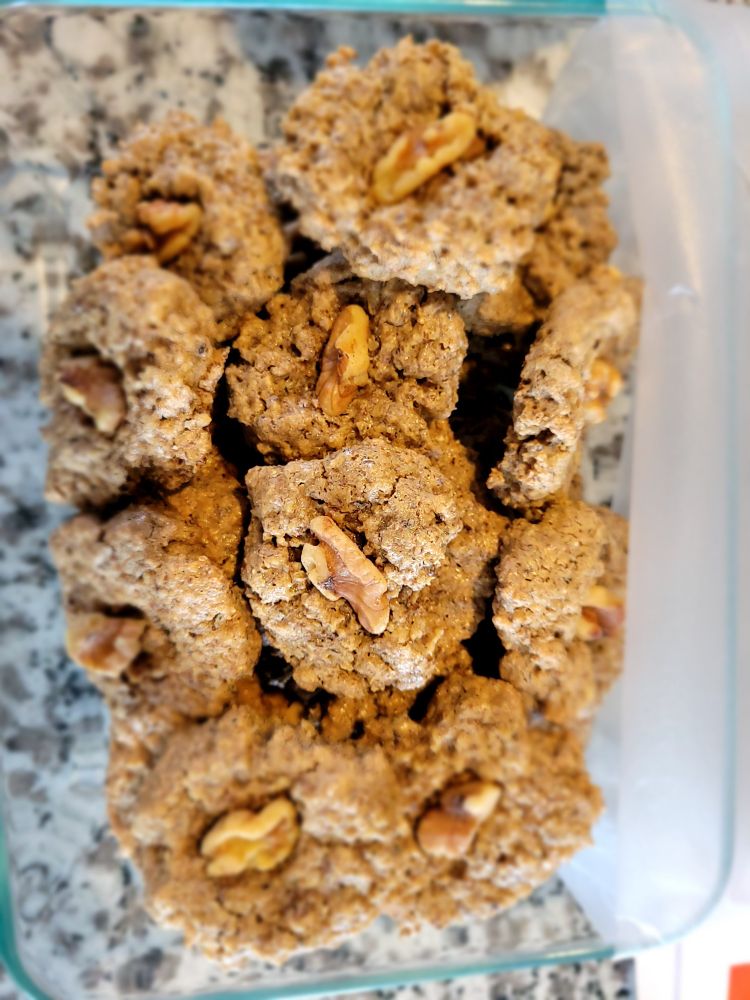 Homemade brown circular cookies with a walnut piece on top. Made with ground walnuts, sugar, egg whites, vanilla, cinnamon, and lemon juice.