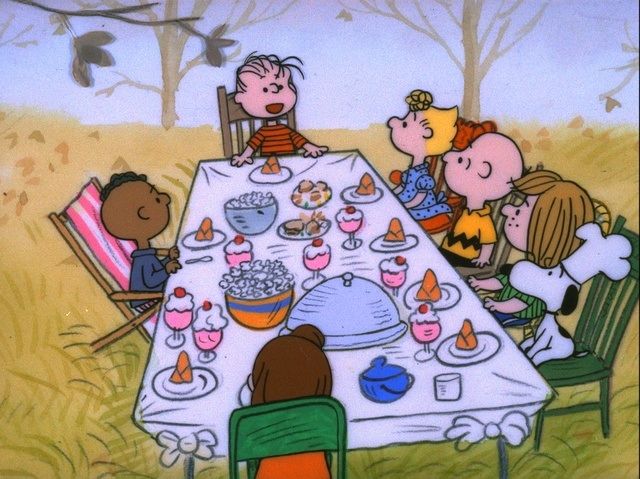 A still from A Charlie Brown Thanksgiving with the kids sitting around the table with their unconventional Thanksgiving dinner.