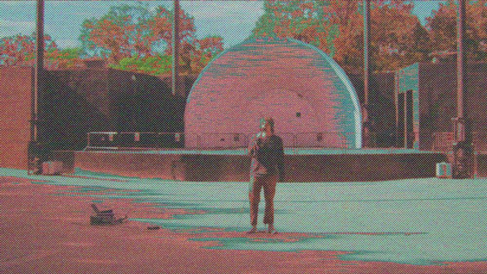 a distorted image of a person in front of a bandshell stage outdoors