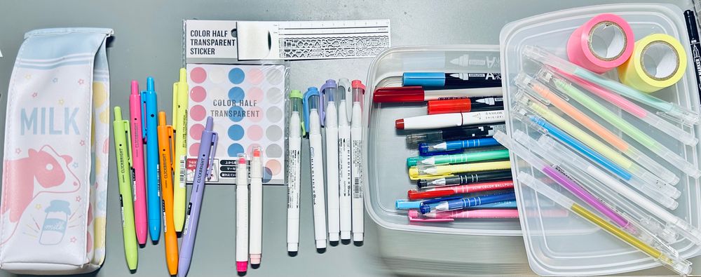Recently I purchased a ton of new pens, markers and highlighters. I was making stickers. There’s a plastic container filled with pens. I have post it note wasbi tape. 