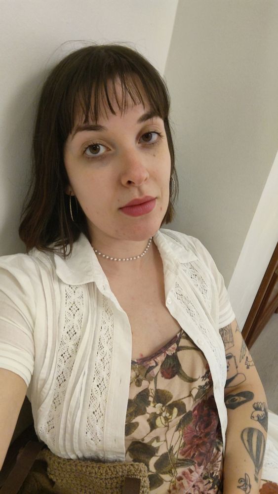 mulher de 29 anos com pele com textura - manchas, olheiras, espinhas. cabelo curto com franja, usando brincos de argola, gargantilha de pérolas, uma camisa, vestido de seda estampado. 