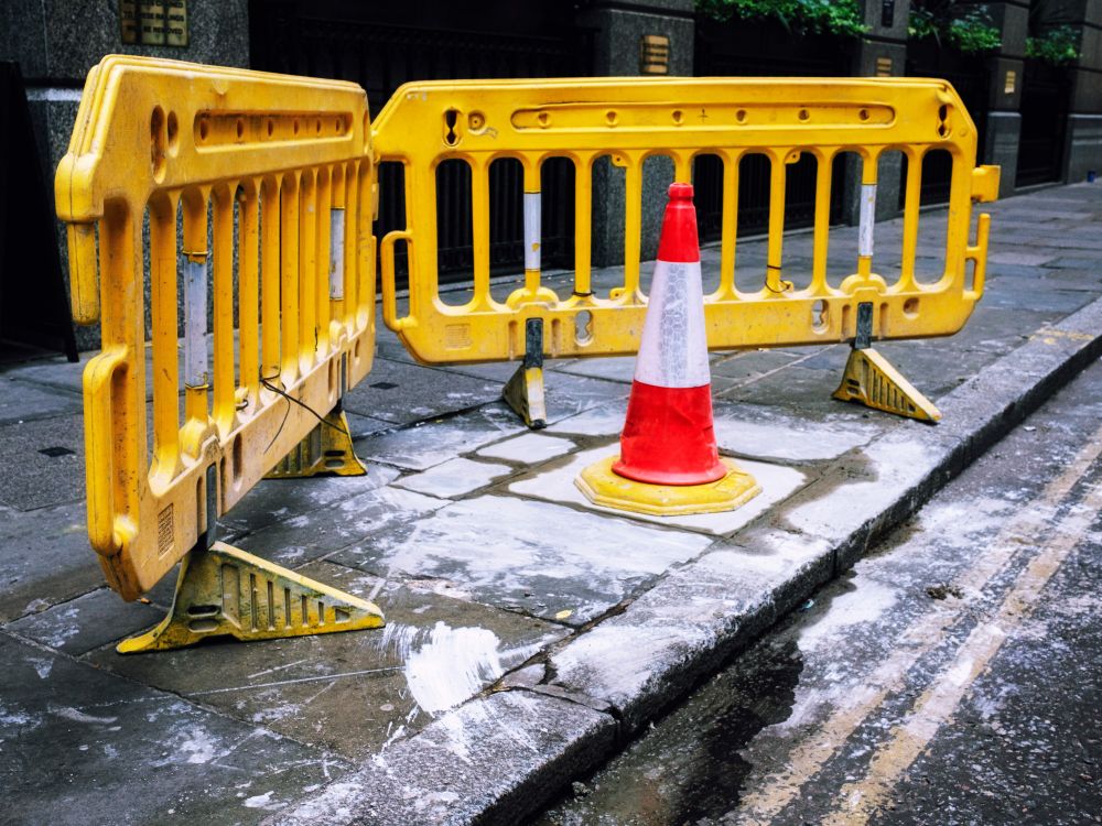 A vivid photograph of a traffic cone on a pavement covered in paint with a yellow guard rail.