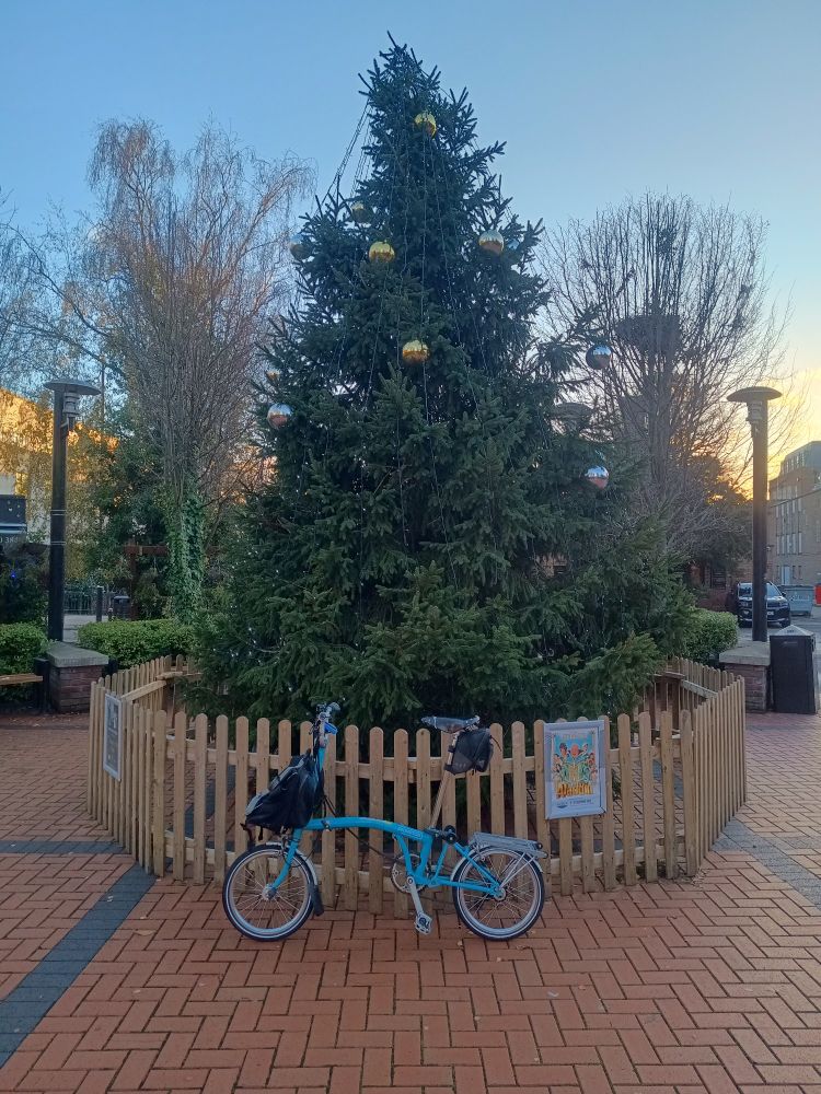 A tall Christmas tree with a blue bike in front of it