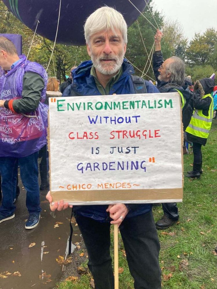 A protestor holding a sign reading “Environmentalism without class struggle is just gardening.”