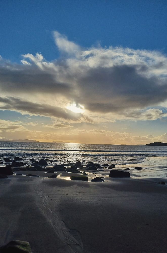 Image taken at the end of Mulranny beach, Mayo. The sun is a little below half way in the sky peeping behind a cloud. The sun reflects water like a halo. 