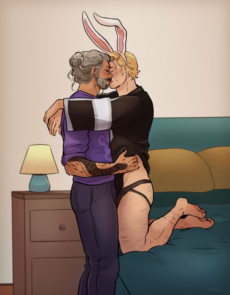 Stede kneeling on the bed in a jersey and a jock strap, wearing bunny ears on his head, kissing Ed who is standing next to the bed in a purple shirt and jeans, with his hands lifting Stede’s jersey and holding his side