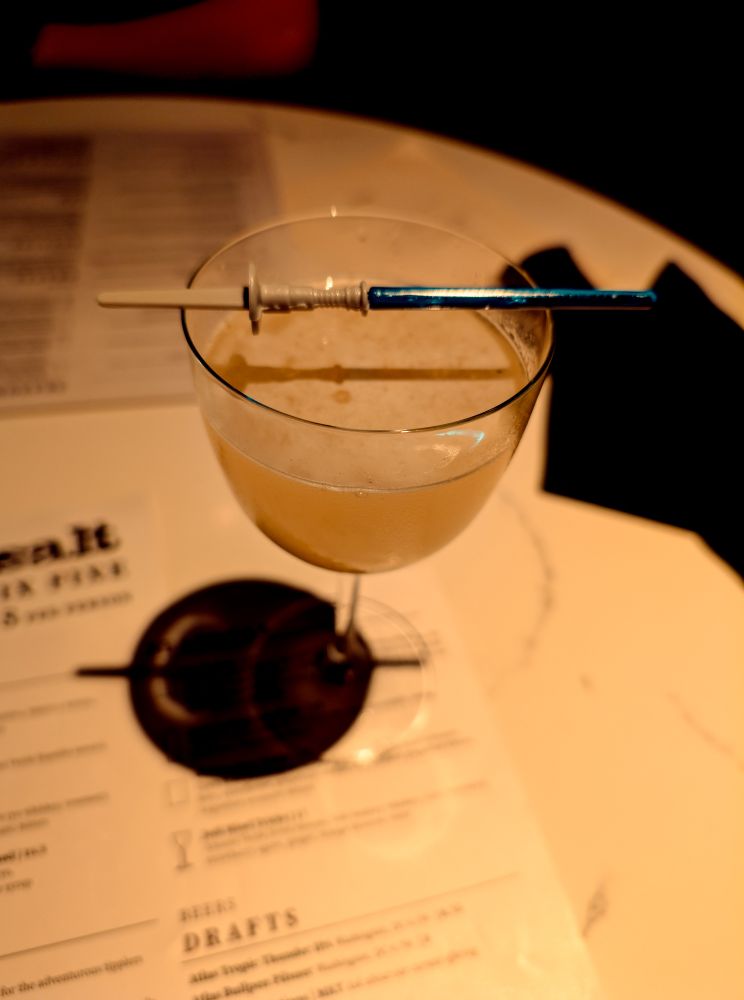 A cocktail with a novelty plastic lightsaber pick laid across the rim of the glass